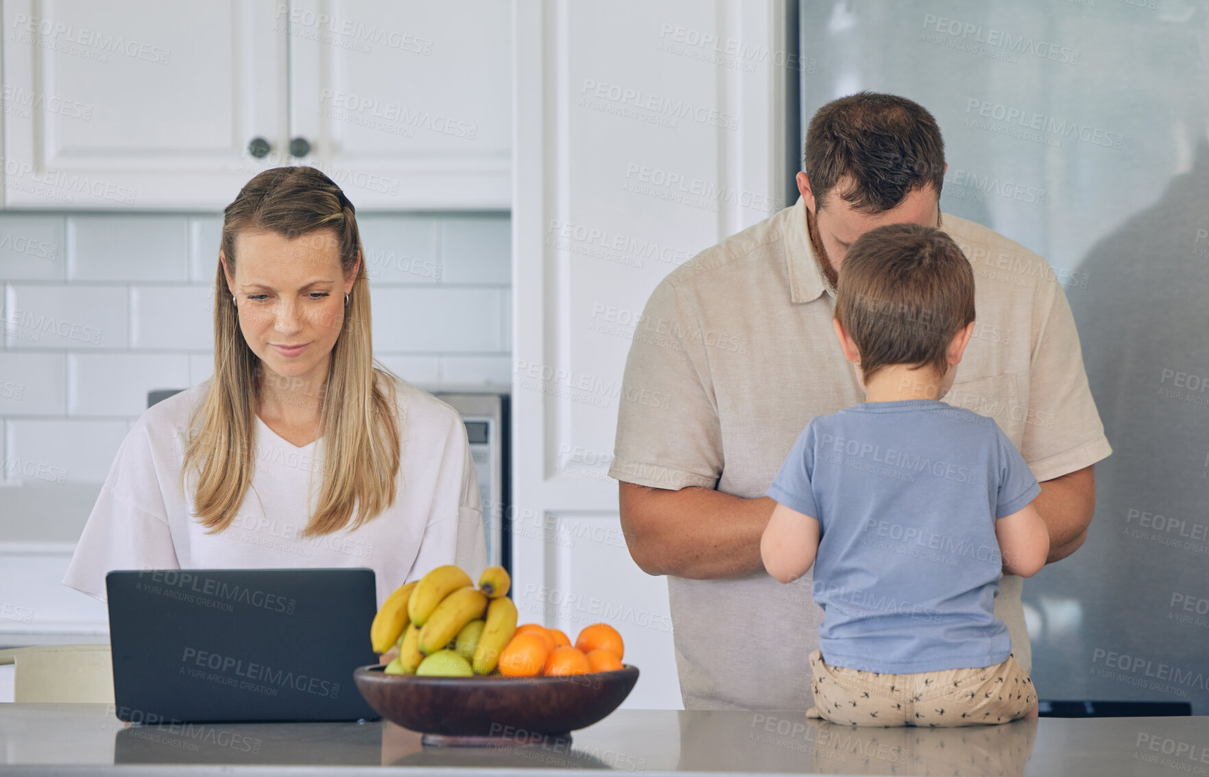 Buy stock photo Happy young caucasian family having lunch time with fresh fruit in a  bright kitchen. Beautiful young mother and father feeding their cute son fruit while using a laptop at home