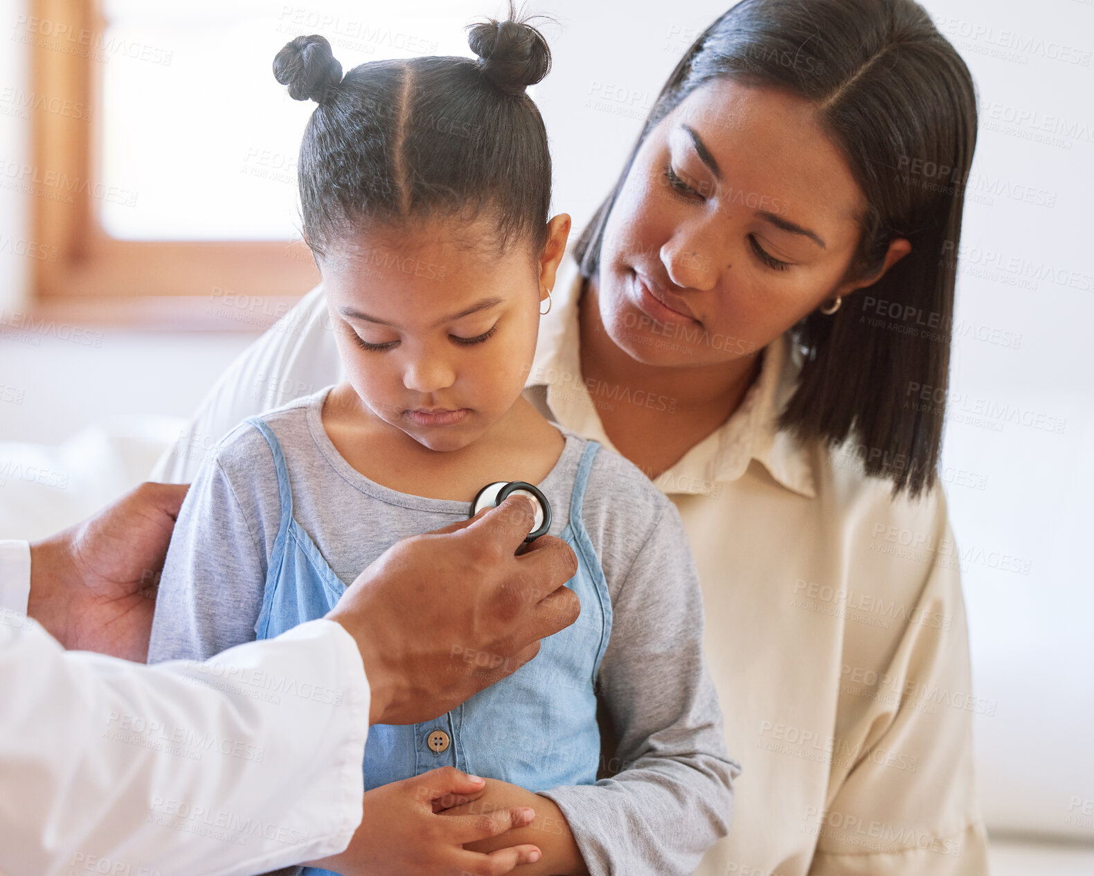 Buy stock photo Sad little girl at doctor's office. Sick girl sitting with mother while male paediatrician listen to chest heartbeat. Male doctor examining child with stethoscope. Mom holding kid during doctor visit