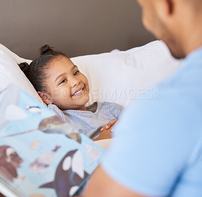 Buy stock photo A cute little smiling mixed race girl laughing while lying in bed and enjoying story time. Young father reading his adorable african American daughter a bedtime story while she relax in bed at home 