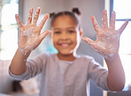 Little girl washing hands with water and soap in a bathroom. Happy kid showing soapy palms. Hand hygiene and virus protection. African American girl smiling while playing with foam from soapy hands 