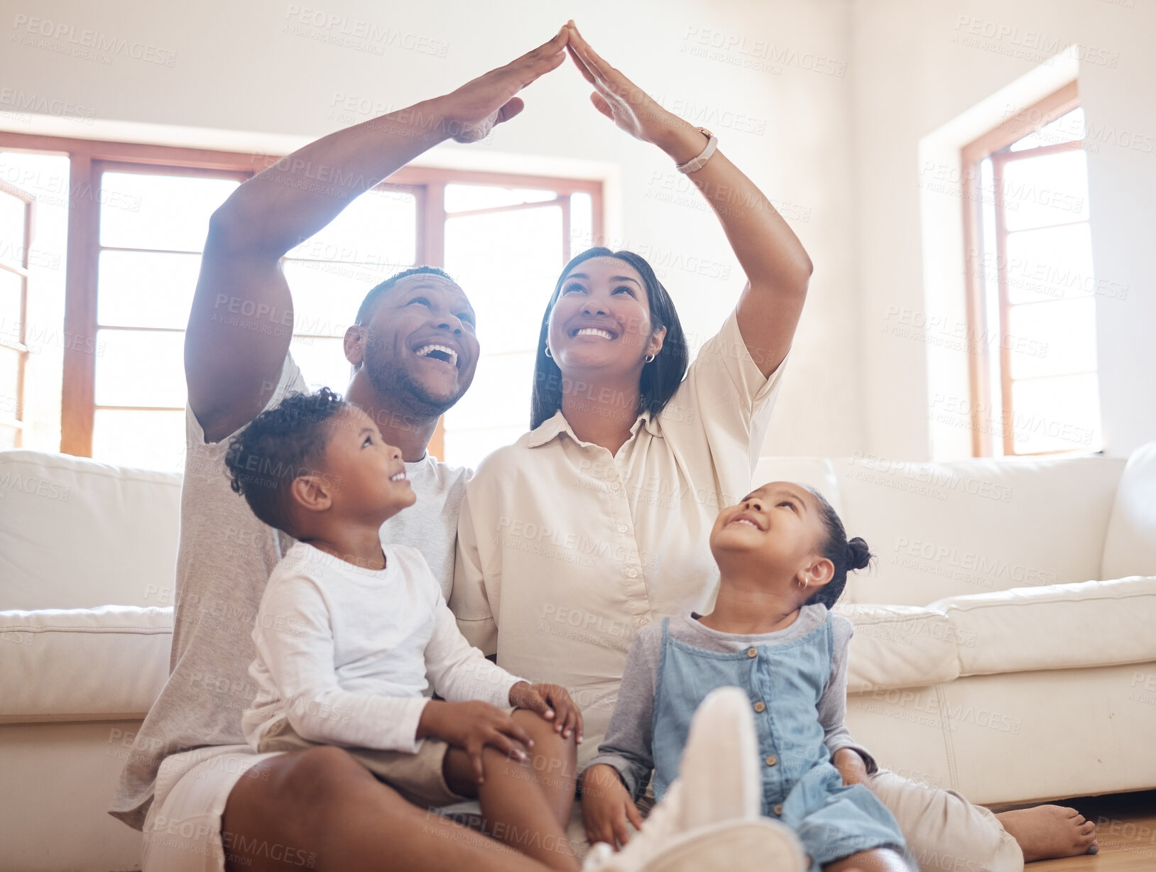 Buy stock photo Stylish mixed race parents with two kids sitting on floor, mom and dad making roof figure with hands arms over heads of adorable son and daughter inside their new house
