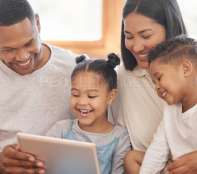 Happy mixed race smiling family of four bonding on a sofa while streaming movies on the internet using a digital tablet at home. Young couple looking cheerful with their daughter and son