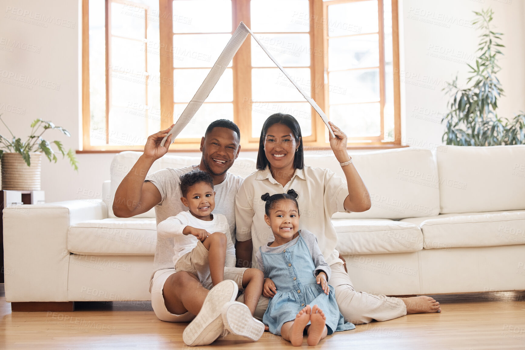 Buy stock photo Cheerful parents with two kids smiling and keeping roof mockup over heads in new home. Mixed race family with son and daughter sitting on floor in cozy living room during relocation