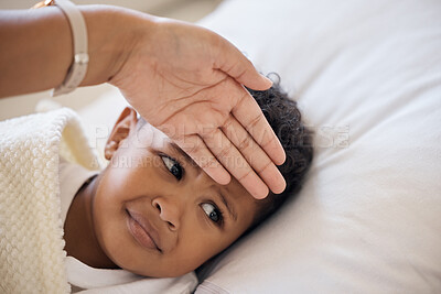 Closeup shot of a cute mixed race little boy feeling unwell and looking while lying in bed at home. Young mother feeling the temperature of her sick child while lying on a sofa