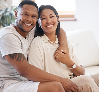 Buy stock photo Portrait of smiling mixed race couple sitting together at home. Loving and affectionate man sitting with his arm around his wife relaxing on the couch at home 