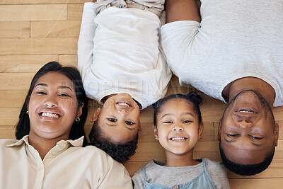 Portrait of smiling mixed race family of four from above lying and relaxing on wooden floor at home. Carefree loving parents bonding with daughters. Young girls spending quality time with mom and dad