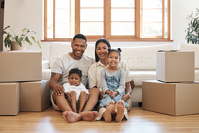Portrait of happy young family with two kids sitting in new home, stacked cardboard boxes in living room. Mixed race couple with children buying property, moving house or apartment