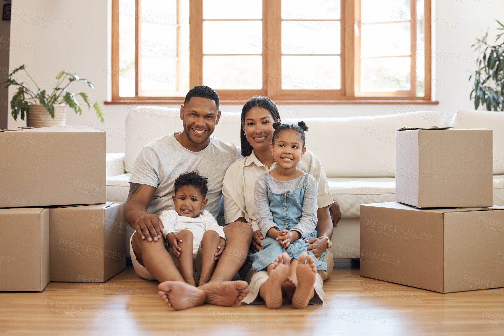 Buy stock photo Portrait of happy young family with two kids sitting in new home, stacked cardboard boxes in living room. Mixed race couple with children buying property, moving house or apartment
