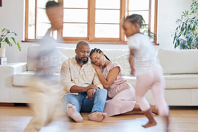 Buy stock photo Tired African American couple sitting on the lounge floor looking tired and drained while their energetic children plays around them. Two black siblings having fun while their exhausted parents relax