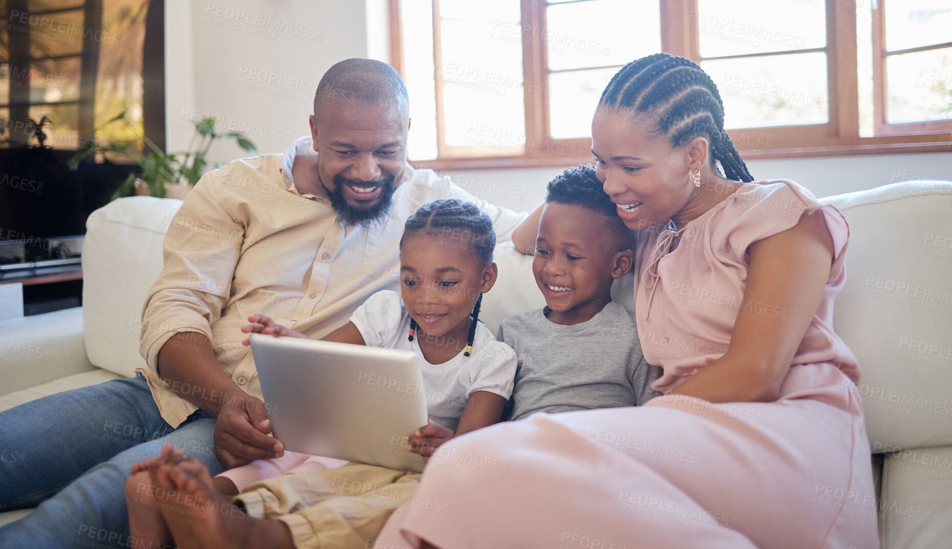 Buy stock photo A young african american family sitting on the sofa together and smiling while using a tablet at home