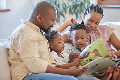 A young african american family sitting on the sofa together and smiling while reading a story book at home