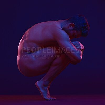 Full length man posing nude and crouching while isolated against a dark studio background. Strong and muscular athlete showing naked body in creative, artistic studio. Sexy hot model feeling sensual