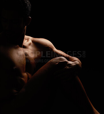 Alluring man posing in a dark studio. Naked multiracial man sitting posing. Sensual male model posing. Muscular nude man in a studio. Elegant,naked unknown hispanic man isolated on black background