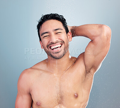 Portrait of one sexy muscular young mixed race man taking refreshing hot shower against blue studio background. Fit smiling guy washing hair and body with clean running water for good hygiene routine