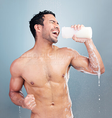 Buy stock photo One sexy muscular young mixed race man singing in the shower against a blue studio background. Fit guy having fun with a bottle of soap or shampoo as a pretend mic during his daily body care routine