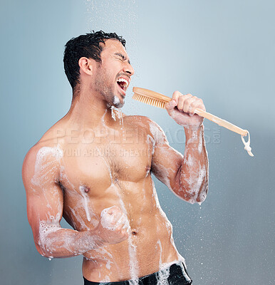 Buy stock photo One young muscular mixed race man singing in the shower against a blue studio background. Cheerful hispanic guy having fun with a shower brush as a mic doing his morning hygiene routine in the shower