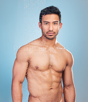 Buy stock photo Portrait view of a sexy muscular man showering alone and looking serious against a blue studio background. Fit and strong mixed race man standing under pouring water. Hispanic athlete enjoying hot shower