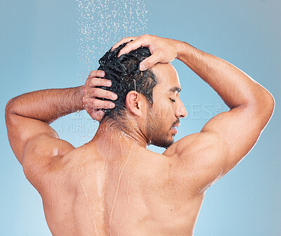 Buy stock photo Rear view of a muscular man showering alone in a studio and washing his hair against a blue background. Fit and strong mixed race man standing under pouring water. Hispanic athlete enjoying hot shower