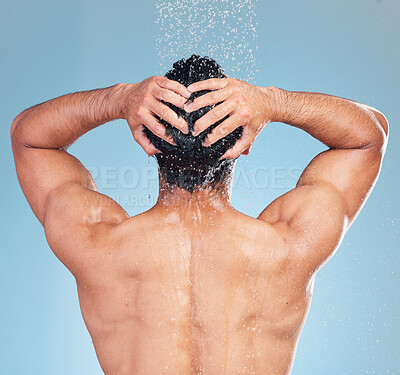 Buy stock photo Rear view of a muscular man showering alone in a studio and washing his hair against a blue background. Fit and strong mixed race man standing under pouring water. Hispanic athlete enjoying hot shower