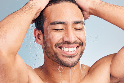 Buy stock photo Smiling muscular asian man showering alone in a studio and washing his hair against a blue background. Fit and strong mixed race man standing under pouring water. Hispanic athlete enjoying hot shower