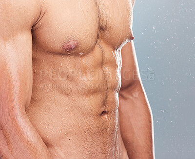 Closeup of clean water running down a muscular mixed race man's sexy toned chest with six pack abs during a refreshing hot shower for daily hygiene and body care routine against a studio background