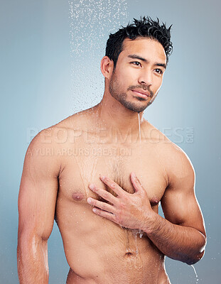 Buy stock photo A handsome muscular man showering alone in a studio and washing his body against a blue background. Fit and strong mixed race man standing under pouring water. Hispanic athlete enjoying hot shower