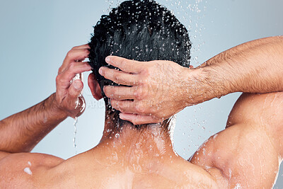 Buy stock photo Rear view of a muscular man showering alone in a studio and washing his hair against a blue background. Fit and strong mixed race man standing under pouring water. Hispanic athlete enjoying hot shower