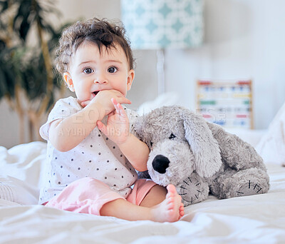 Portrait of cute caucasian baby girl playing with soft fluffy toy on bed in bedroom. Little adorable infant girl sucking her finger looking curious