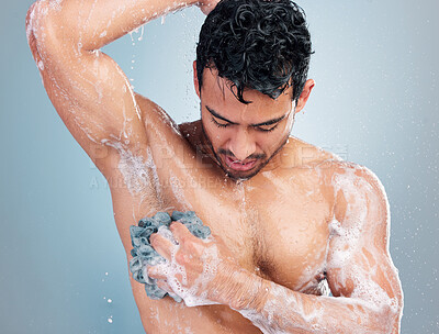 Buy stock photo Young mixed race man taking a warm shower washing his underarms with a wash cloth against a blue studio background. Hispanic guy washing his body with soap under clean running water for good hygiene