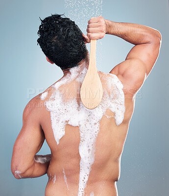 Buy stock photo Closeup of man taking a warm shower washing his back with a shower brush against a blue studio background. Mixed race male washing his body with soap scrubbing his back doing morning grooming routine