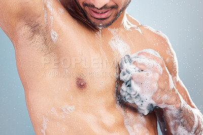 Buy stock photo Closeup of one muscular mixed race man taking refreshing hot shower against blue studio background. Fit sexy guy using soap and loofah to wash and scrub body with clean running water for good hygiene