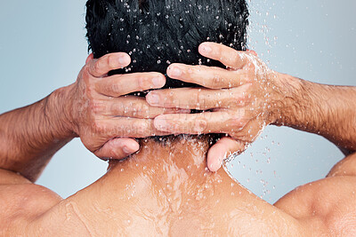 Buy stock photo Rearview closeup of ethnic man showering alone in a studio and washing hair against a blue background. Fit and strong mixed race man standing under pouring water. Hispanic athlete enjoying hot shower