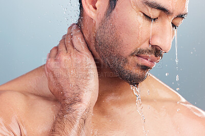 Close up of a muscular man showering alone in a studio and washing his hair against a blue studio background. Fit and strong mixed race man standing under pouring water. Hispanic athlete having hot shower