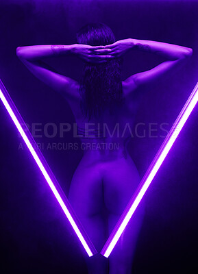 Nude woman posing in studio isolated on black behind two purple neon lights. Sexy naked mixed race woman posing seductively between two beams of light in the shape of a V exposing her buttocks against a black studio background