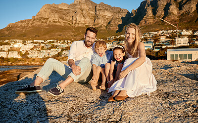 Portrait of a caucasian family watching the sunset sitting on a rock together on the beach. Parents spending time with their son and daughter on holiday. Siblings bonding with mom and dad on vacation