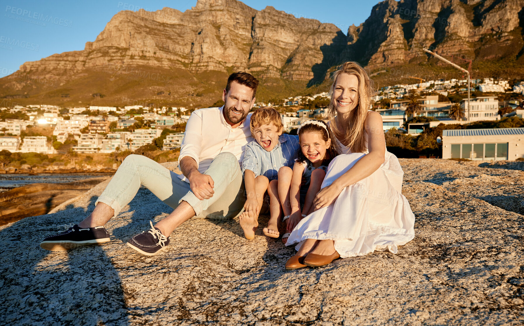 Buy stock photo Portrait of a caucasian family watching the sunset sitting on a rock together on the beach. Parents spending time with their son and daughter on holiday. Siblings bonding with mom and dad on vacation