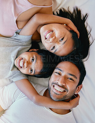 Buy stock photo Happy family lying on the bed. Portrait of happy family from above. Multiracial family resting in bed together. Happy girl relaxing with her parents. Young parents bonding with their daughter
