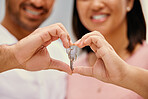 Closeup of a mixed race couple smiling making a heart gesture with their hands holding a key in their new house together. Loving hispanic husband and wife happy to be moving into their own home
