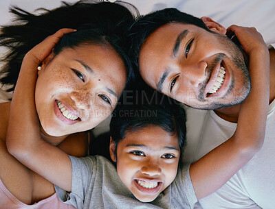 Happy mixed race family lying on the bed. Portrait of happy family from above. Multiracial family resting in bed together. Happy girl relaxing with her parents. Young parents bonding and showing affection with their daughter