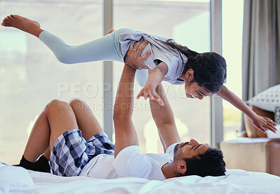 Buy stock photo Dad lifting daughter in the air while lying on bed. Young father playing with adorable little daughter and enjoying a family weekend together. Loving and caring dad practising acroyoga with child