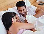 Adorable little hispanic girl smiling while lying and playing in bed with her parents. Mixed race family with one child relaxing and bonding in the morning while still lying in bedroom