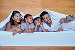 Happy family in bed. A young hispanic family in bed taking a selfie using a smartphone. Two parents bonding with their daughters at home. Sisters relaxing with their mother and father under bed sheets