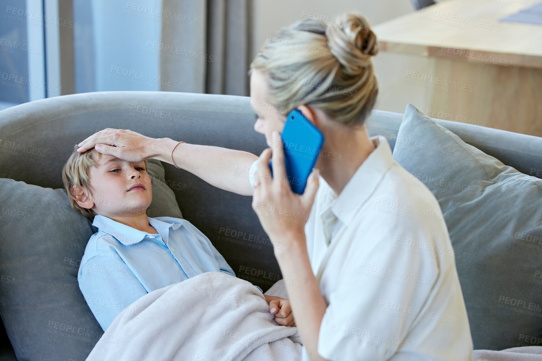 Buy stock photo Sick boy on sofa with mom on the phone. Young caucasian mother calling the doctor and feeling her ill son's forehead while he lies under a blanket on the couch at home. He has a fever and temperature