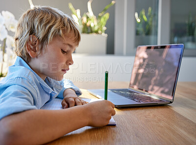 Young homeschool little boy sitting alone and using laptop to study. Caucasian child writing and learning remotely due to covid pandemic. Kid studying online classes with technology through video call