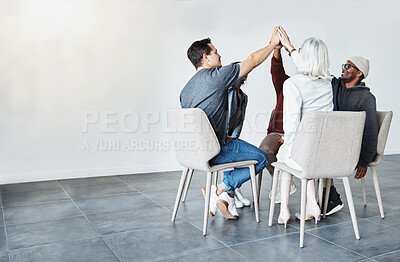 Diverse group of businesspeople giving each other a high five sitting on chairs in a meeting in an office at work. Happy women and men joining their hands celebrating success together while working