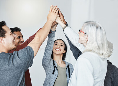 Diverse group of five businesspeople smiling giving each other a high five in a meeting in an office at work. Happy women and men joining their hands in unity standing together while working
