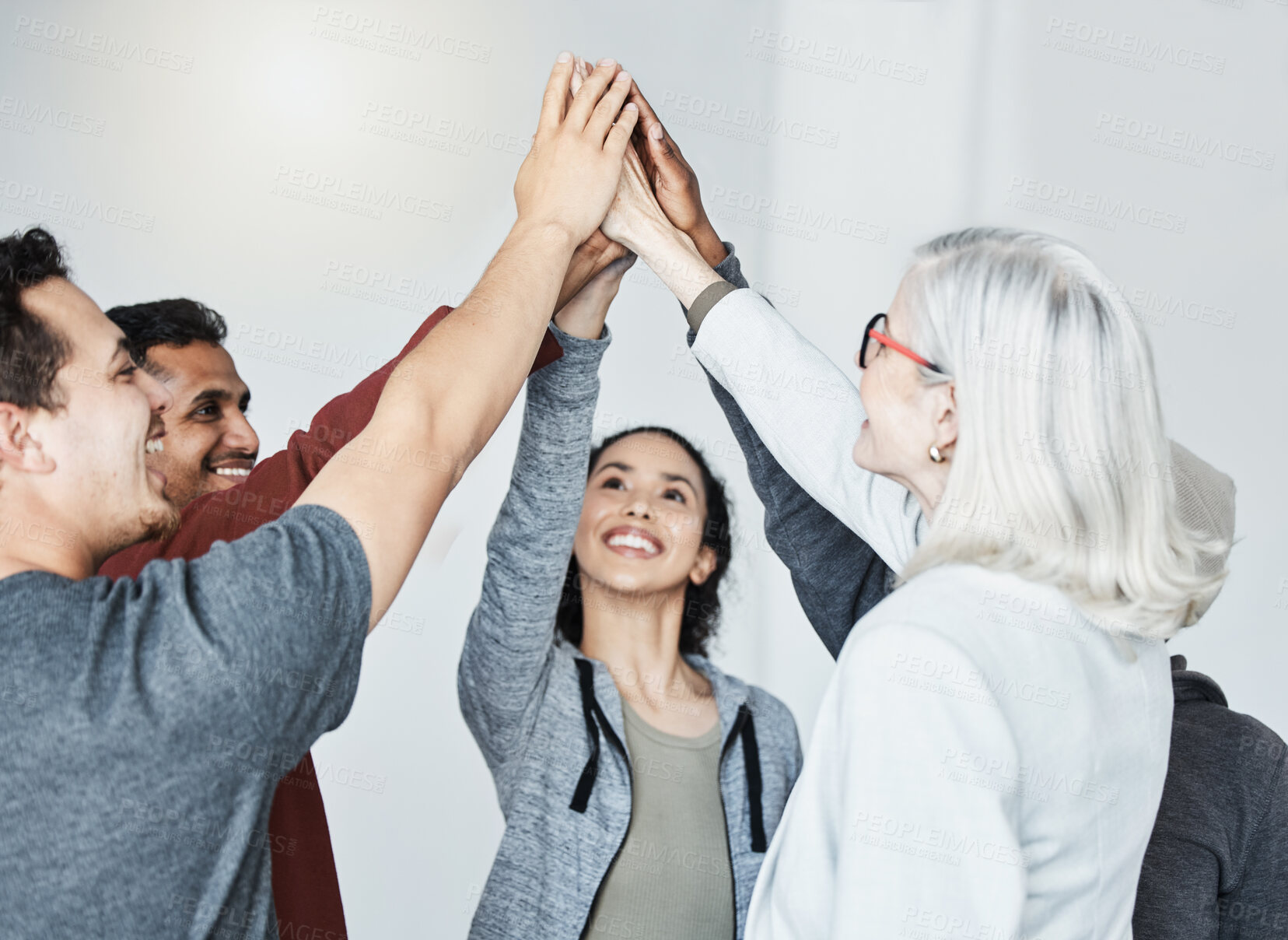 Buy stock photo Diverse group of five businesspeople smiling giving each other a high five in a meeting in an office at work. Happy women and men joining their hands in unity standing together while working