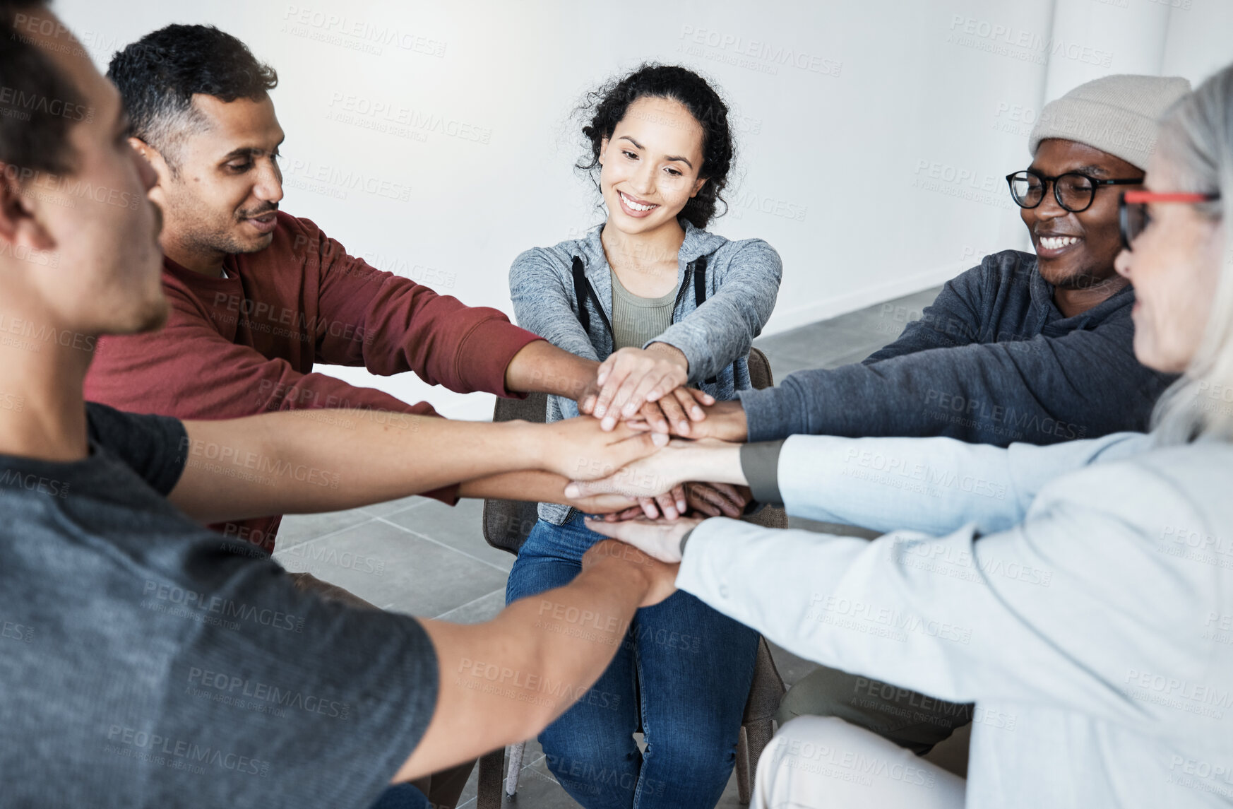 Buy stock photo Diverse group of people sitting together in a circle and stacking their hands in the middle after therapy. Smiling support group celebrating after a successful session. Friends support mental health