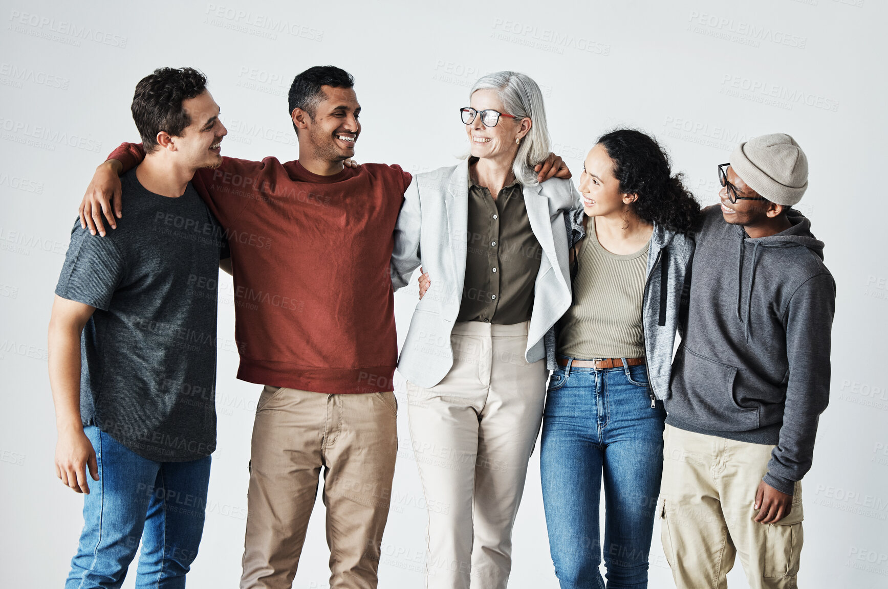 Buy stock photo Team of happy united young business people hugging each other. Diverse mixed race group of men and women standing in row in their office, huddling and smiling all together. Unity and teamwork against a grey background