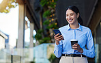Young mixed race happy businesswoman using social media on a phone while drinking a cup of coffee. One hispanic woman smiling while typing a message on her phone and standing in the city
